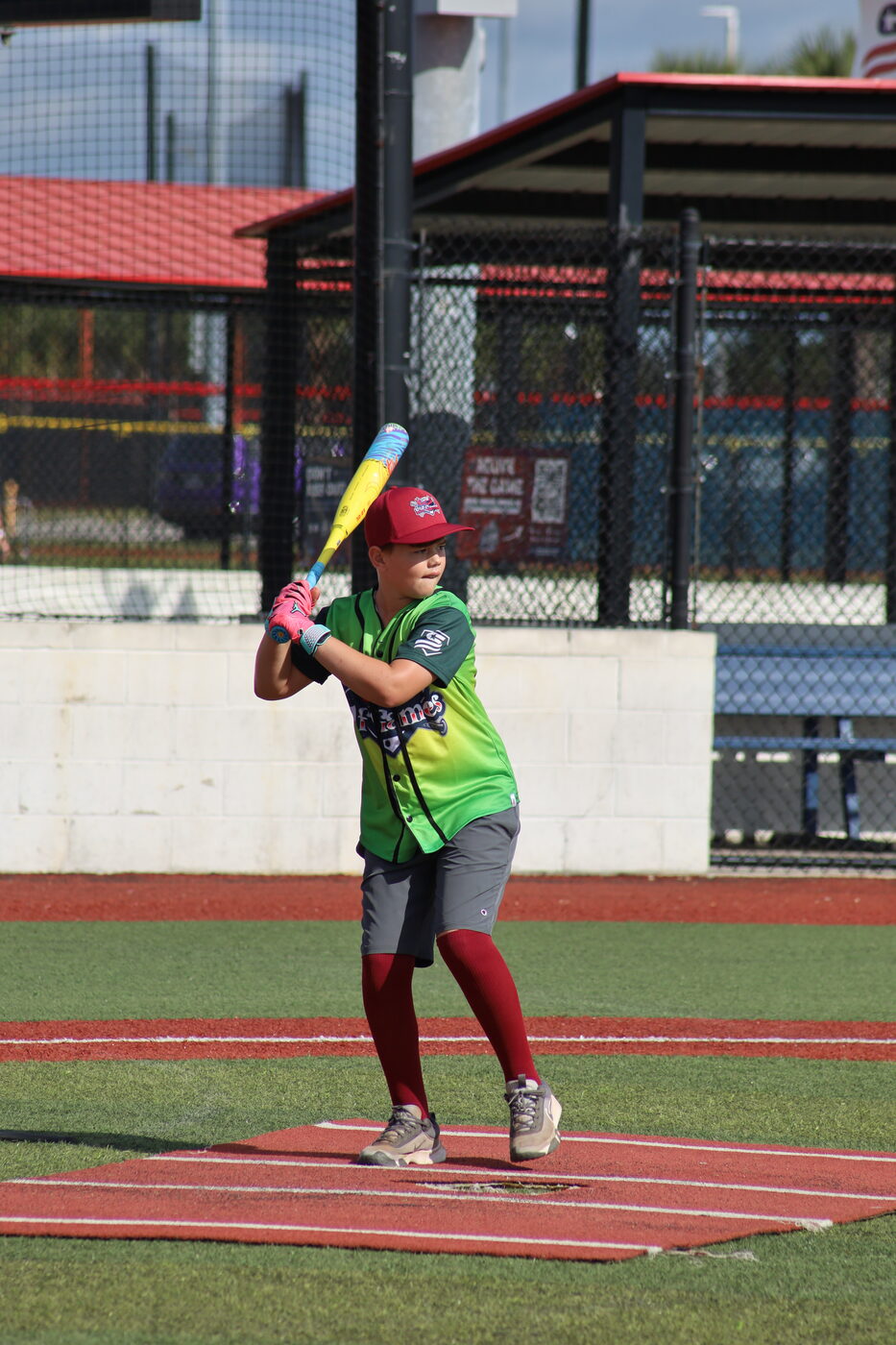 Young batter in a green Elf Games jersey standing in the batter's box, ready for the pitch.